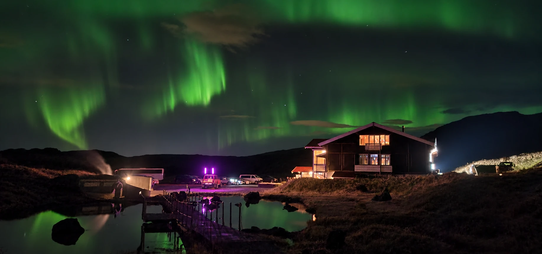 Green aurora above the geothermal valley and illuminated Hveradalir lodge